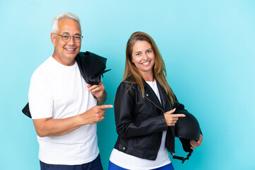 Middle age bikers couple with a motorcycle helmet isolated on blue background pointing finger to the side in lateral position