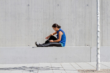 Young woman sitting on wall reading digital tablet