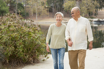 Senior couple walking along pathway, holding hands, laughing