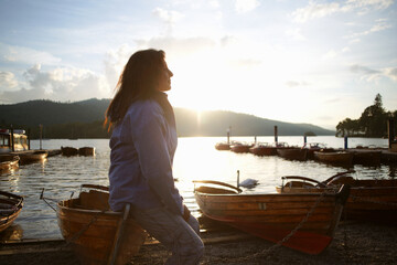 Fototapeta premium Mature woman sitting on canoe by lake, Lake District, Cumbria, UK