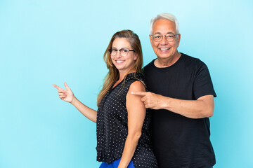 Middle age couple isolated on blue background pointing finger to the side and presenting a product