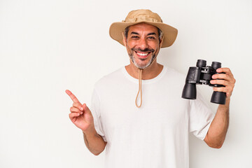 Middle age caucasian man holding binoculars isolated on white background  smiling and pointing aside, showing something at blank space.