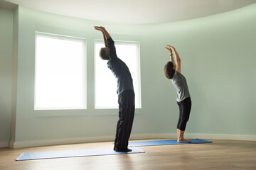 Side view of mature couple reaching upwards stretching arms bending backwards