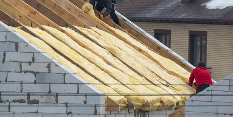 Roofer builder worker installing roof insulation material on new house under construction © Smole