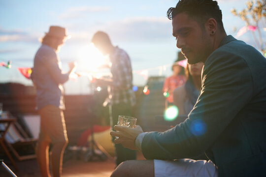 Man sitting alone with drink at early evening party