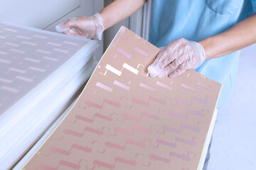 High angle view of young man wearing latex gloves sorting sheets of flexible circuits