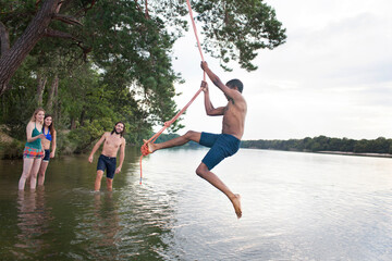 Young man rope swinging above lake © Image Source Limited