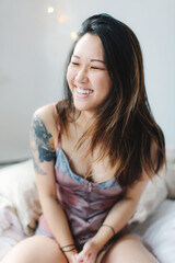 Naklejka premium Portrait of young woman, sitting on bed, laughing