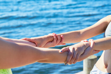 Cropped view of women in front of ocean holding into each others wrists