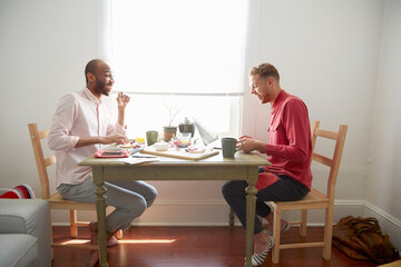 Side view of men sitting at dining table having breakfast laughing