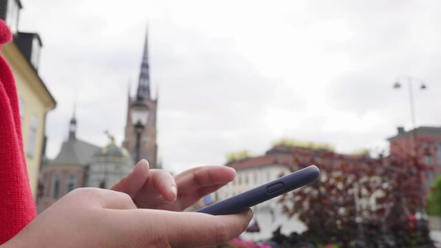 Close up hands of asian woman standing and using smartphone in town, going out for a walk to visit beautiful city in Sweden. Traveling abroad on long holiday concept