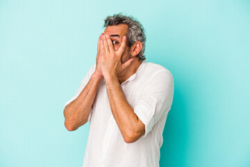 Middle age caucasian man isolated on blue background  blink through fingers frightened and nervous.
