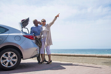 Senior couple standing beside car with open boot, near beach