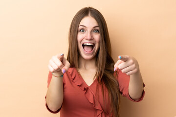 Young caucasian woman isolated on beige background surprised and pointing front