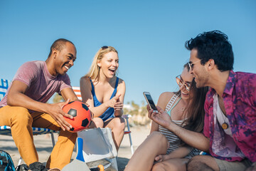 Adult friends reading smartphone texts on beach, Santa Monica, California, USA