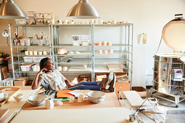 Woman in pottery workshop feet up looking away