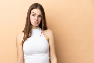 Obraz premium Young caucasian woman isolated on beige background with sad expression