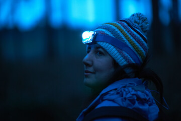 Female hiker wearing head torch looking over her shoulder from forest at night