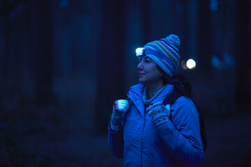 Female hiker wearing head torch hiking through forest at night