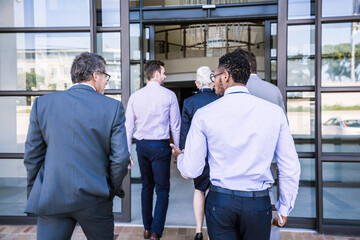 Rear view of businessmen and woman arriving at office building