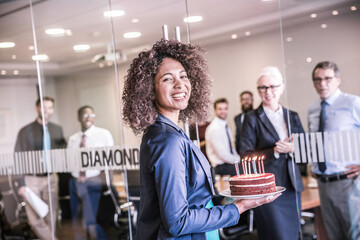 Portrait of young businesswoman carrying celebration cake into boardroom