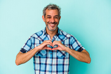 Middle age caucasian man isolated on blue background  smiling and showing a heart shape with hands.