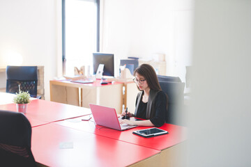 Young woman at office desk typing on laptop