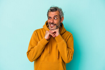 Middle age caucasian man isolated on blue background  praying for luck, amazed and opening mouth looking to front.