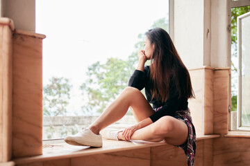 Young woman gazing from window sill of abandoned house, Victoria Peak, Hong Kong