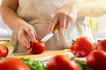 Chef slicing tomato using knife on the table in restaurant. Process of cutting and preparation food in kitchen.