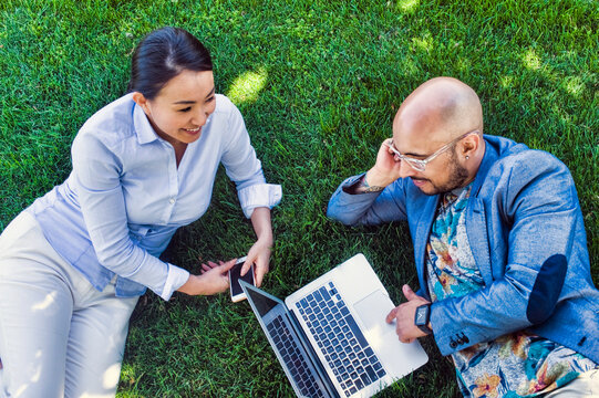 Businessman and woman sitting outdoors on grass, using laptop