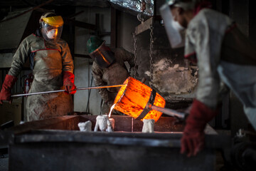 Metalworkers working in foundry, pouring molten bronze