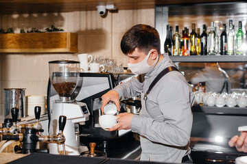 A masked barista prepares delicious coffee at the bar in a cafe. The work of restaurants and cafes during the pandemic.