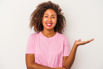 Young african american woman with curly hair isolated on white background showing a copy space on a palm and holding another hand on waist.