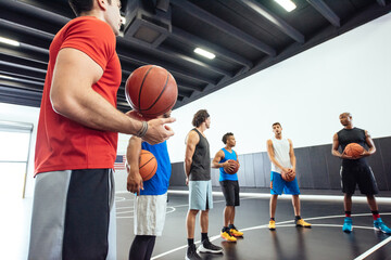 Male trainer and basketball team practicing on court holding ball