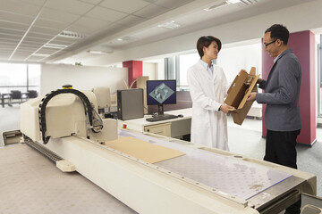 Technician showing cardboard box to manager by packaging machine in printing and packaging factory, China