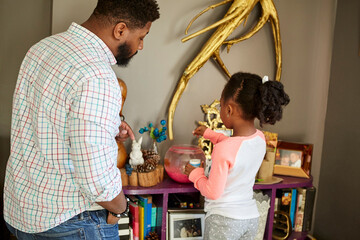 Father watching daughter feed fish in goldfish bowl
