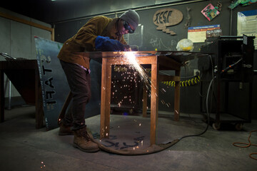 Male metalsmith plasma cutting metal at workbench