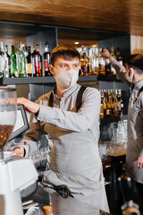 Two masked baristas prepare delicious coffee in the cafe bar. The work of restaurants and cafes during the pandemic.