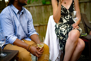 Man and woman at garden party, sitting, in conversation, holding wine glasses, mid section