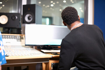 Rear view of young male college student at sound mixer in recording studio