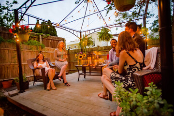 Group of people at garden party, sitting on decking, in conversation