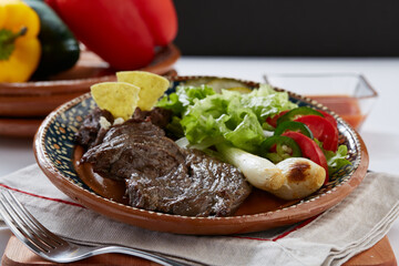 Arrachera servida con frijoles negros refritos, totopos y ensalada