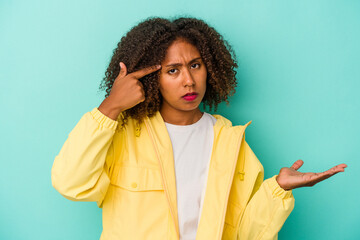 Young african american woman with curly hair isolated on blue background holding and showing a product on hand.