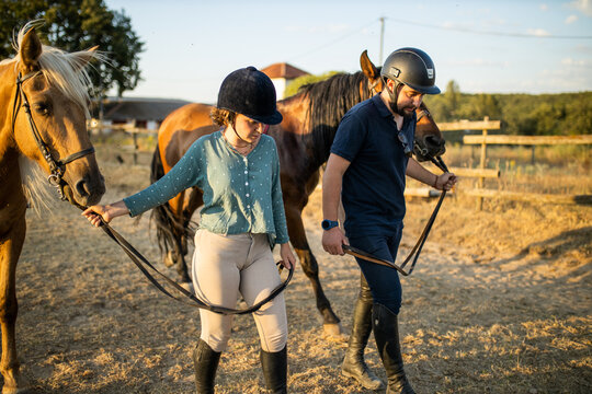 Woman and trainer walking with horses in countryside paddock