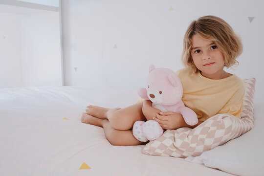 Girl with toy bear resting on bed in house