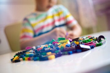 Fototapeta premium Hands of a child constructing Bricks against the background of a heap of multicolored constructor blocks.