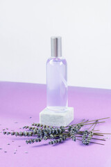 Obraz na płótnie Canvas Lavender water or hydrolat in glass bottle with lavender flowers on podium on purple table. Aromatherapy concept. Mock up