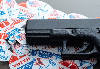 Concept for election violence with handgun placed on many torn and damaged voting stickers or...