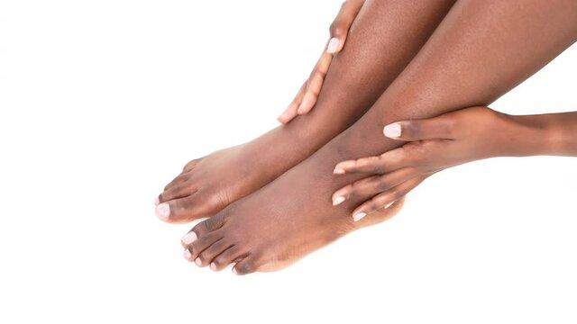 Close up of black woman's hands massaging her feet and legs. Isolated on a white background.